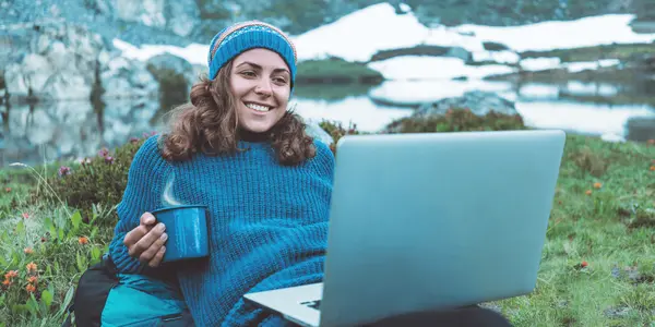 Kvinna som sitter i  naturen och bedriver distansstudier