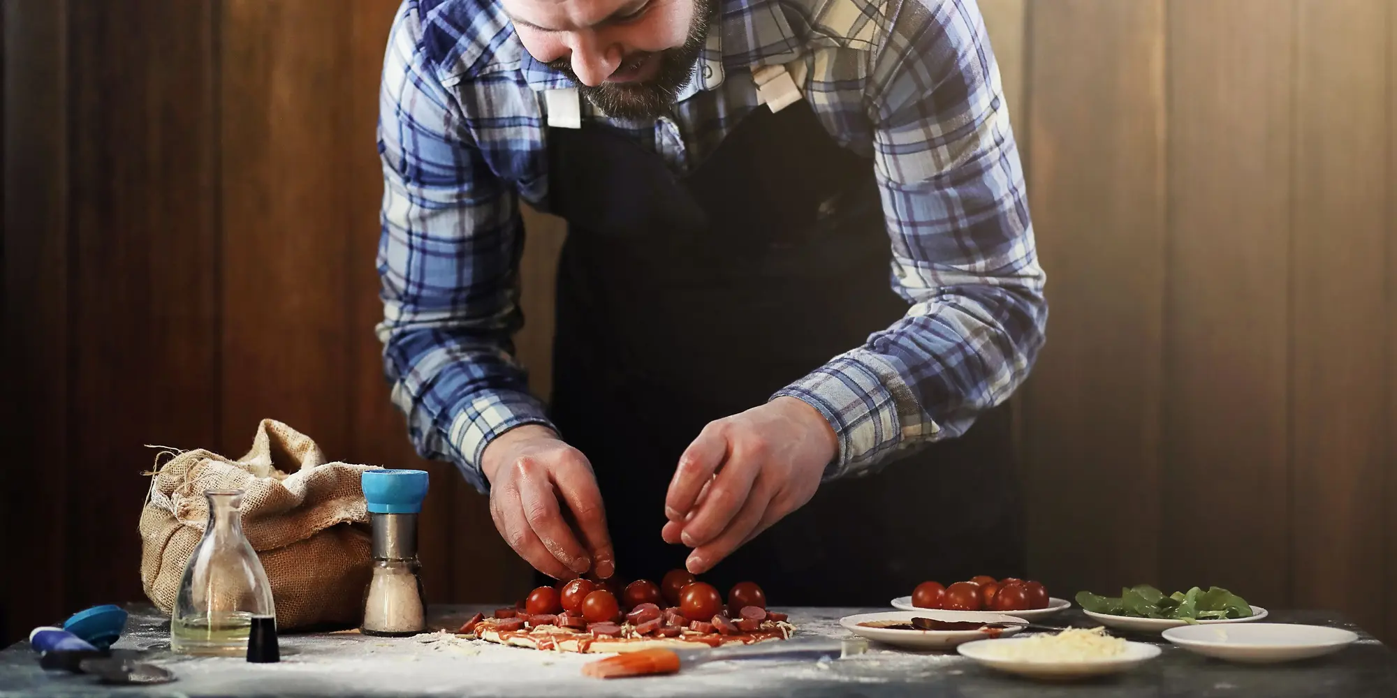 En man står vid en köksbänk och toppar en pizza