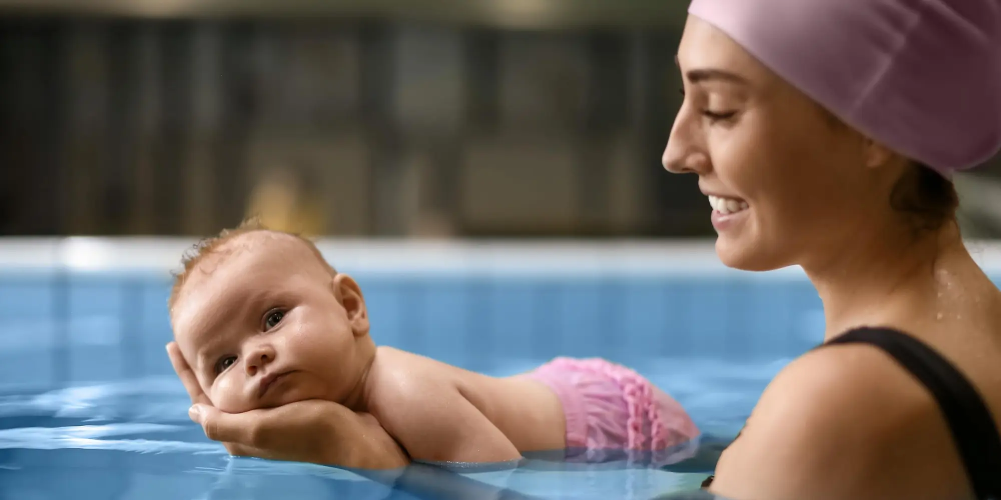 mamma håller i sin bebis i simbassäng